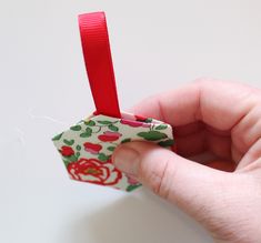 a hand is holding a small ornament with red ribbon on the top and bottom