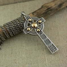 a silver and gold celtic cross necklace on a piece of wood next to a rope