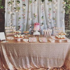 a table topped with cakes and cupcakes next to a wall covered in flowers