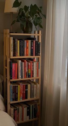 a bookshelf filled with lots of books next to a lamp on a bed