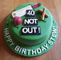 a green cake with the words 40 not out on it and baseball bats, bat, and ball