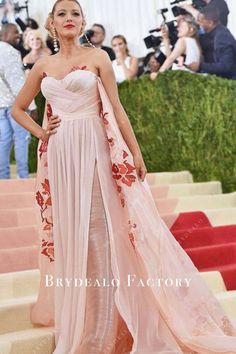 a woman in a pink dress standing next to stairs with people taking pictures behind her