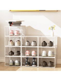 a white shelf filled with lots of shoes next to a vase on top of a hard wood floor