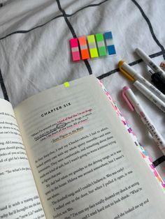 an open book sitting on top of a bed next to markers