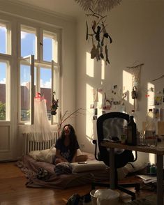 a woman sitting on the floor in front of a window with lots of clutter