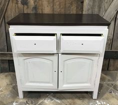 a white cabinet with two doors and brown top on the floor in front of a wooden wall