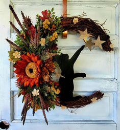 a wreath on the front door with flowers and leaves hanging from it's side