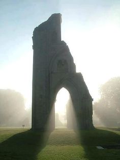 an old stone building in the middle of a field with fog coming from behind it