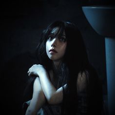 a woman with long black hair standing in the dark