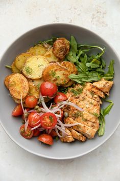 a white bowl filled with meat, vegetables and potatoes on top of a marble table