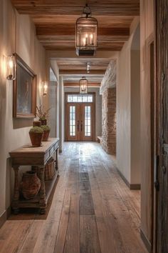 a long hallway with wooden floors and two lanterns hanging from the ceiling, along with potted plants on either side of the door