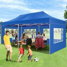 a group of people standing under a blue tent on top of a grass covered field