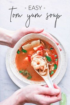 two hands holding a spoon full of soup with shrimp and tortilla in it