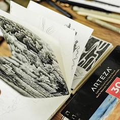 an open book sitting on top of a wooden table next to some pens and pencils