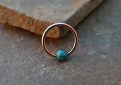 a gold ring with a turquoise bead sits on a rock