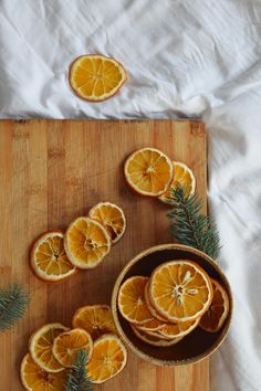 sliced oranges sit on a cutting board next to pine branches