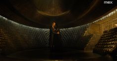 a woman standing in the middle of a room with stacks of wine bottles behind her