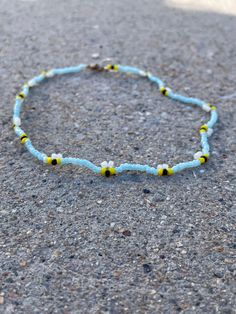 a blue beaded bracelet with yellow and white beads sits on the ground in front of a sidewalk