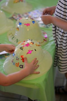 two children are sitting at a table with plates and hats on it, one child is reaching for the plate