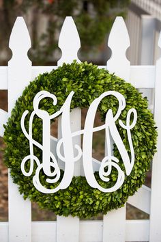 a wreath with the letter m on it is hanging on a white picketle fence