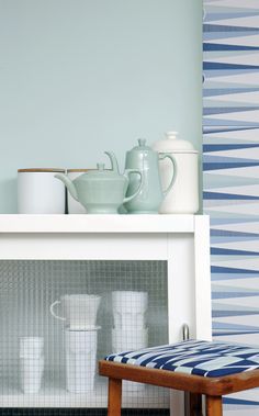 a white shelf with blue and white patterned wallpaper next to a wooden stool in front of it