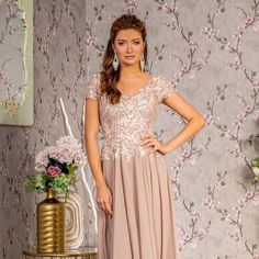 a woman standing in front of a floral wallpaper wearing a dress with sequins on it