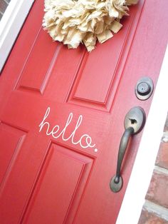 a red door with the word hello written on it and a flower in front of it