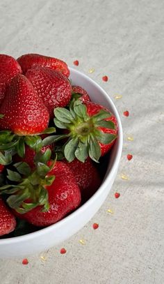 a white bowl filled with lots of strawberries on top of a bed of sprinkles