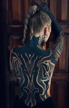 a woman with tattoos on her back standing in front of a door