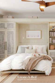 a white bed sitting under a ceiling fan in a bedroom next to a book shelf