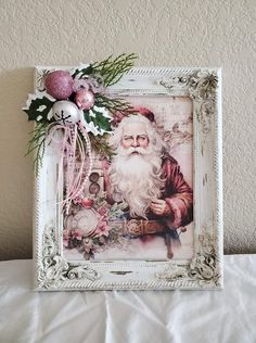 a white frame with a santa clause on it and christmas decorations around the edges, sitting on a bed