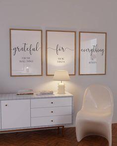 a white chair sitting next to a table with two framed pictures on the wall above it