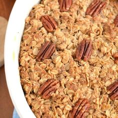 a baked oatmeal in a white dish with pecans and apples behind it