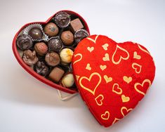 a heart shaped box filled with assorted chocolates on a white table next to a red pillow