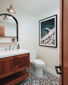 a bathroom with a sink, mirror and toilet in it's corner area next to a painting on the wall