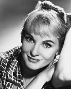 an old black and white photo of a woman with her hand on her head, smiling at the camera