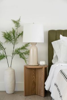 a bedroom with a bed, night stand and plant in the corner next to it