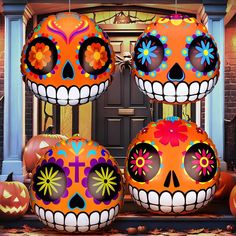 three large pumpkins decorated with brightly colored sugar skulls and flowers are sitting in front of a doorway