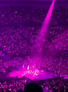 an audience at a concert with purple lighting on the stage and people in the stands