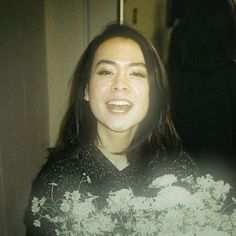 a woman with long hair smiling and wearing a black shirt that has white flowers on it