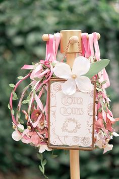 a sign that is on top of a wooden pole with flowers and ribbons around it