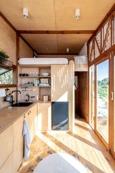 a kitchen with wooden floors and walls has open windows to let in light from the outside