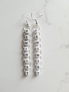 two silver earrings with the word femment spelled in white letters on them sitting on a marble surface