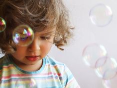 a little boy blowing bubbles in the air with his eyes closed and one eye open