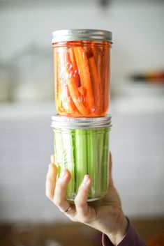 a person holding up a jar full of carrots and celery in it