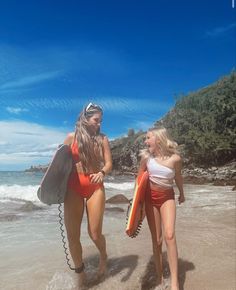 two women walking on the beach with surfboards