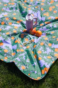 there is a blanket with oranges on it and a cup sitting on the ground