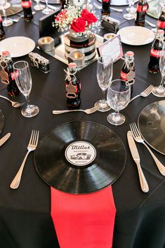 a table set with black and red plates, silverware and wine glasses for an event