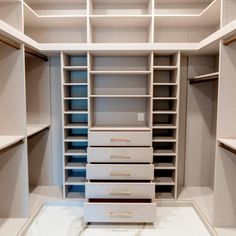 an empty walk in closet with white shelves and drawers