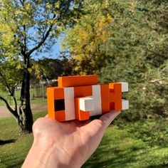 someone is holding up an orange and white object in their hand, with trees in the background